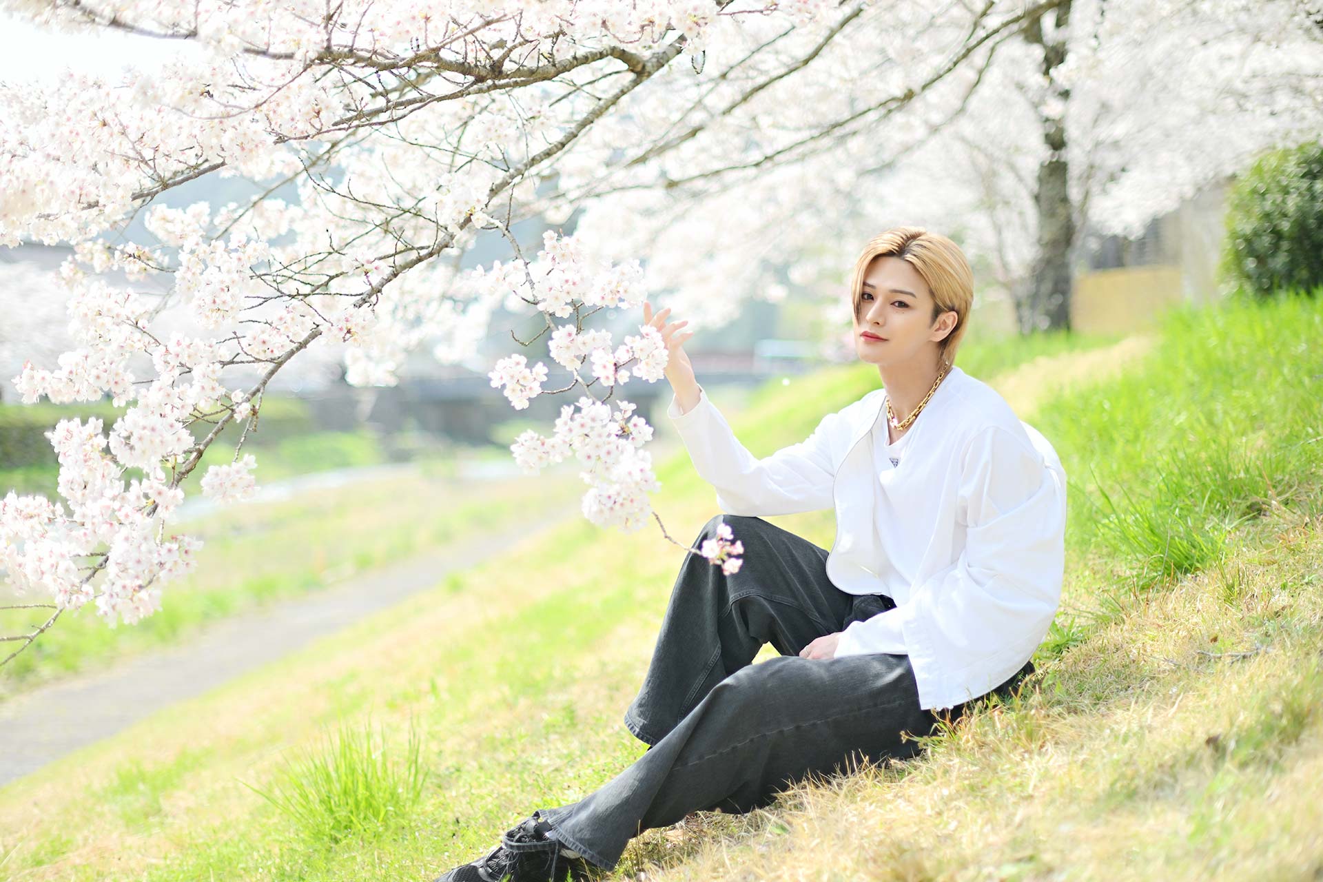 Leo 美月が桜並木のそばの芝生に座りながら花に触れる自然体ショット