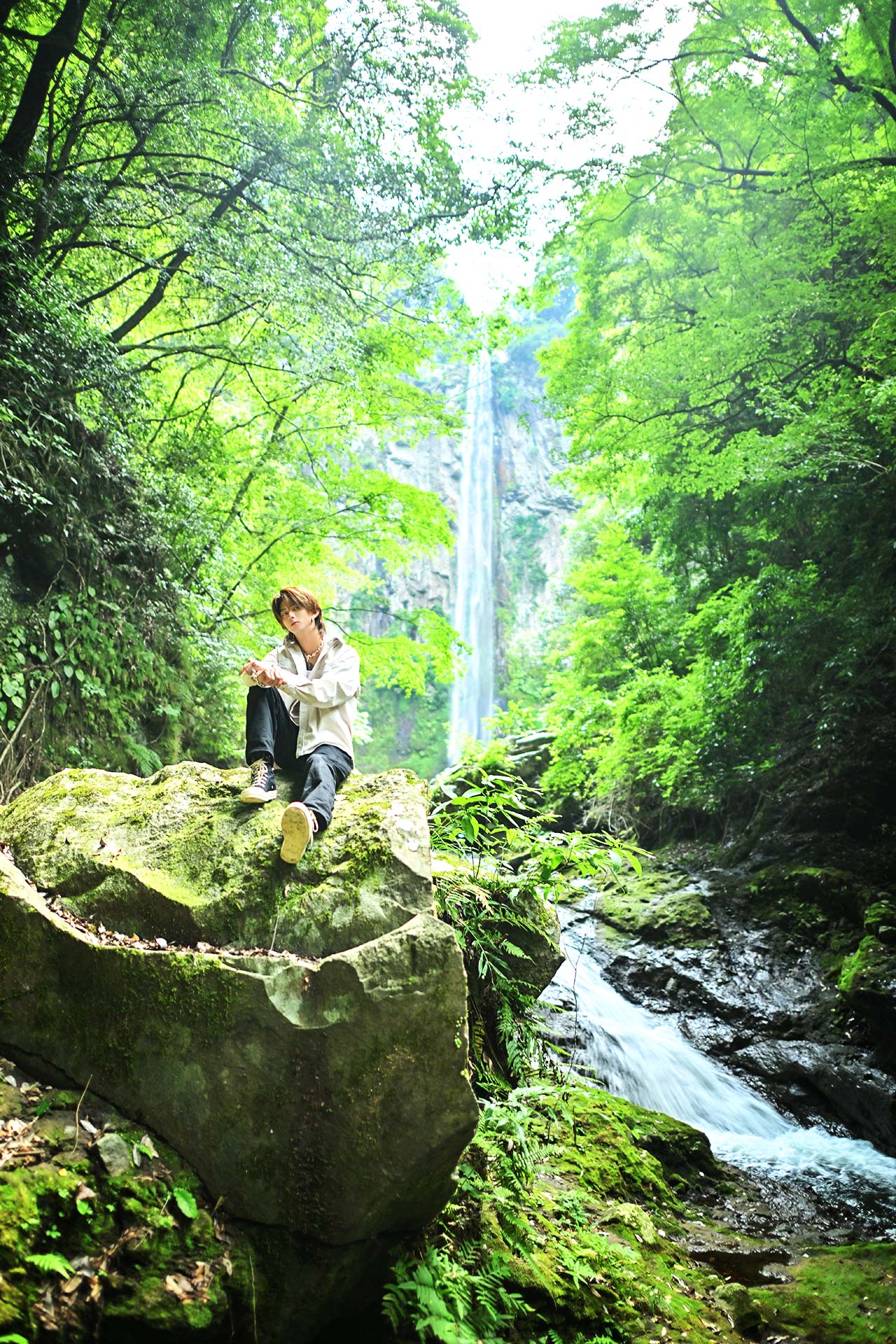 新緑に囲まれた渓流と高く流れ落ちる東椎屋の滝を背景に、大岩へ腰掛けるALF 鬼塚航陽